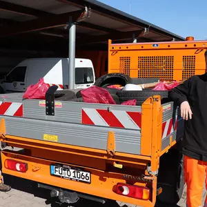 Zwei Männer in Orange neben einem Pritschenwagen mit Abfall und Autoreifen.