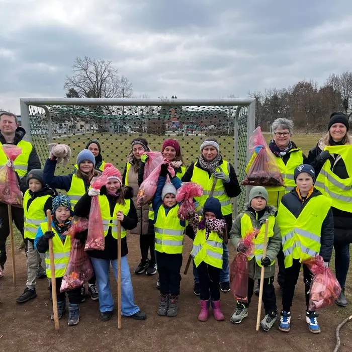 Eine Gruppe von Erwachsenen und Kindern in gelben Warnwesten, die Müll gesammelt haben. Einige halten Tüten in der Hand. 