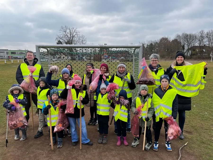 Eine Gruppe von Erwachsenen und Kindern in gelben Warnwesten, die Müll gesammelt haben. Einige halten Tüten in der Hand.