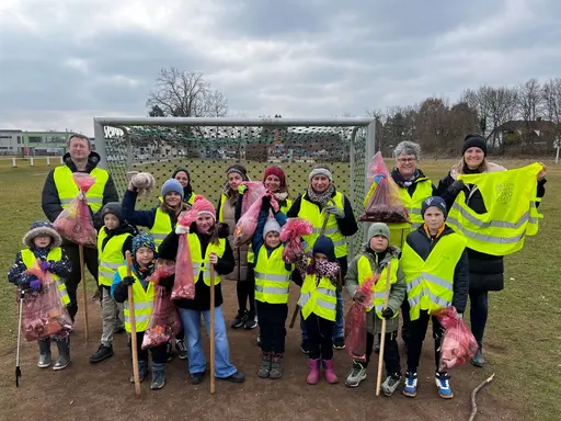 Eine Gruppe von Erwachsenen und Kindern in gelben Warnwesten, die Müll gesammelt haben. Einige halten Tüten in der Hand.