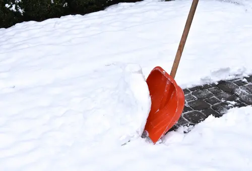 Ein schneebedeckter Gehsteig wird mit einer Schneeschippe geräumt