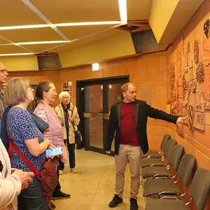 Ein Gruppe Menschen stehen vor dem Ton-Relief. Ein Mann erklärt es.