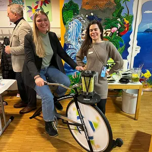 Eine Frau strampelt auf dem Smoothie-Bike und eine weitere steht daneben.