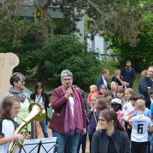 Eine Frau am Mikrofon umringt von Kindern und Erwachsenen