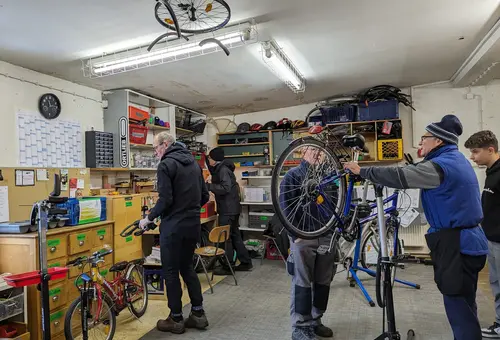 Mehrere Männer und Jugendliche in der Fahrrad-Nachbarschaftswerkstatt bei der Reparatur von Fahrrädern.