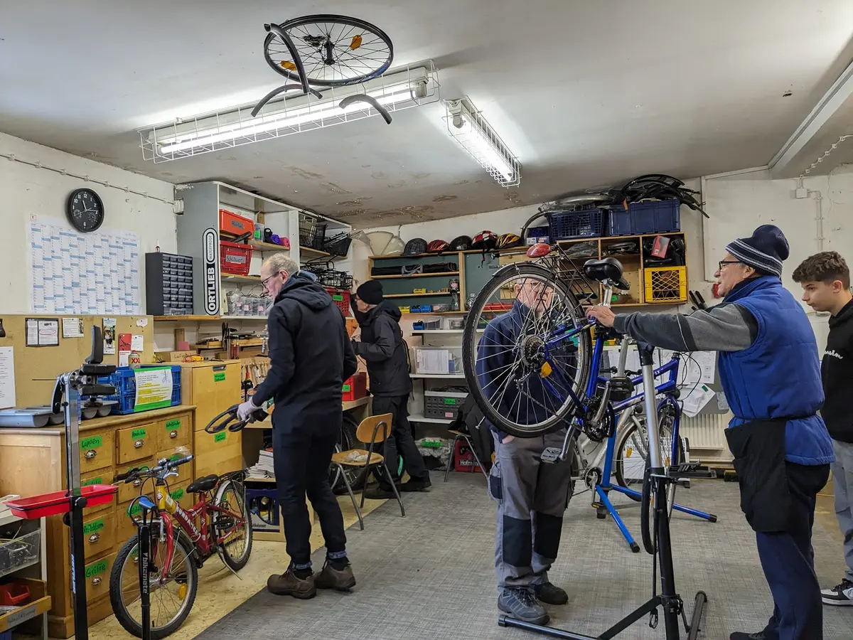 Mehrere Männer und Jugendliche in der Fahrrad-Nachbarschaftswerkstatt bei der Reparatur von Fahrrädern.