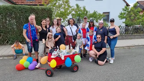 Gruppenbild von Vereinsmitgliedern mit einem mit Luftballons und Luftschlangen dekorierten Bollerwagen
