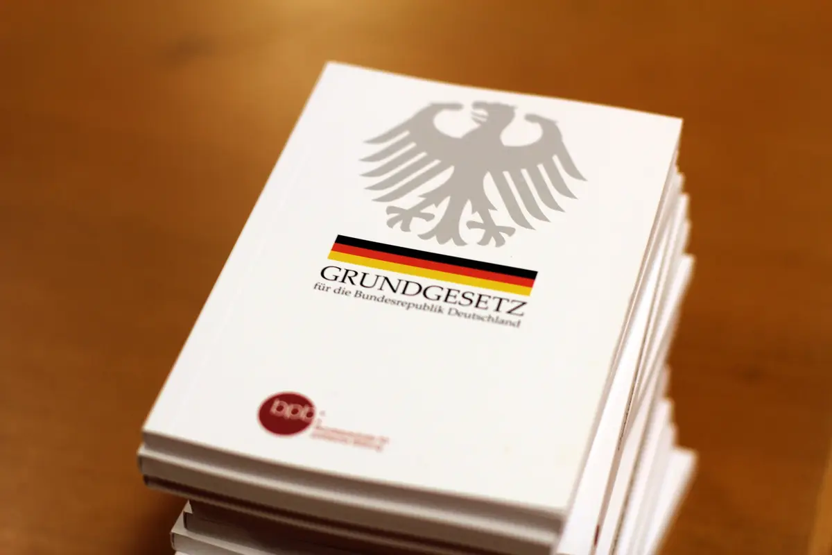 Ein Stapel mit Ausgaben des Grundgesetzes. Auf dem Deckblatt der Bundesadler mit einem schwarz-rot-goldenen Band darunter.