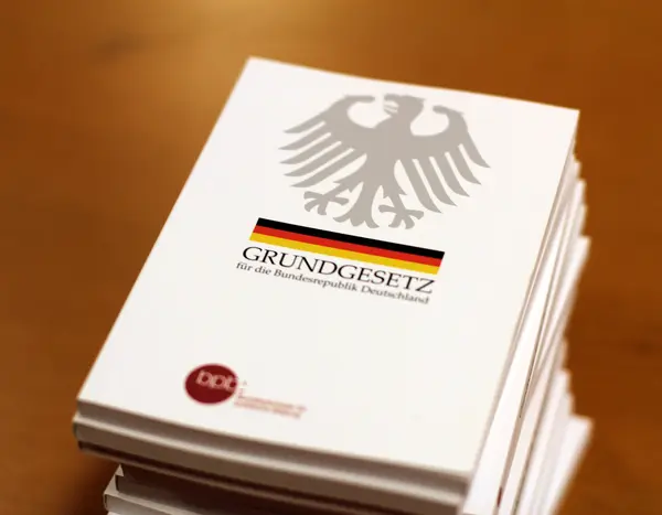 Ein Stapel mit Ausgaben des Grundgesetzes. Auf dem Deckblatt der Bundesadler mit einem schwarz-rot-goldenen Band darunter.
