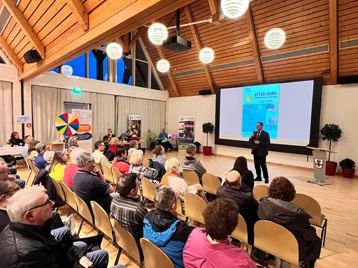 Ein Mann spricht vor einem großen Publikum und hat eine Projektionsfläche im Hintergrund.