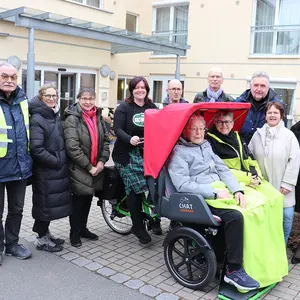 Zwei Personen sitzen in der E-Rikscha und neun weitere Personen vervollständigen das Gruppenbild