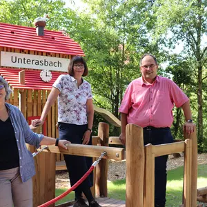Zwei Frauen und ein Mann vor dem neuen "Bahnhof" auf dem Spielplatz in Unterasbach