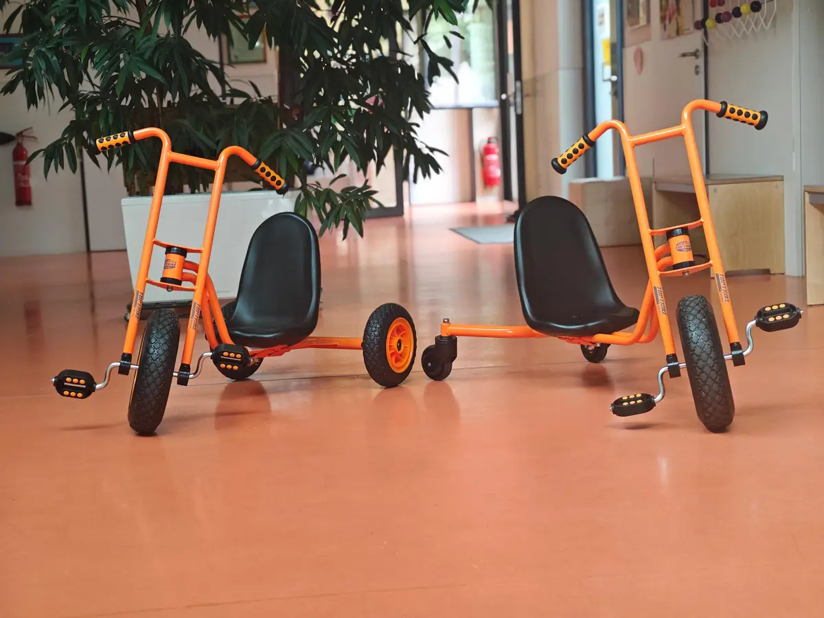 Zwei orangefarbene Dreiräder im Flur.