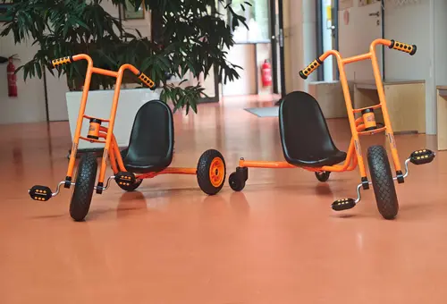 Zwei orangefarbene Dreiräder im Flur.