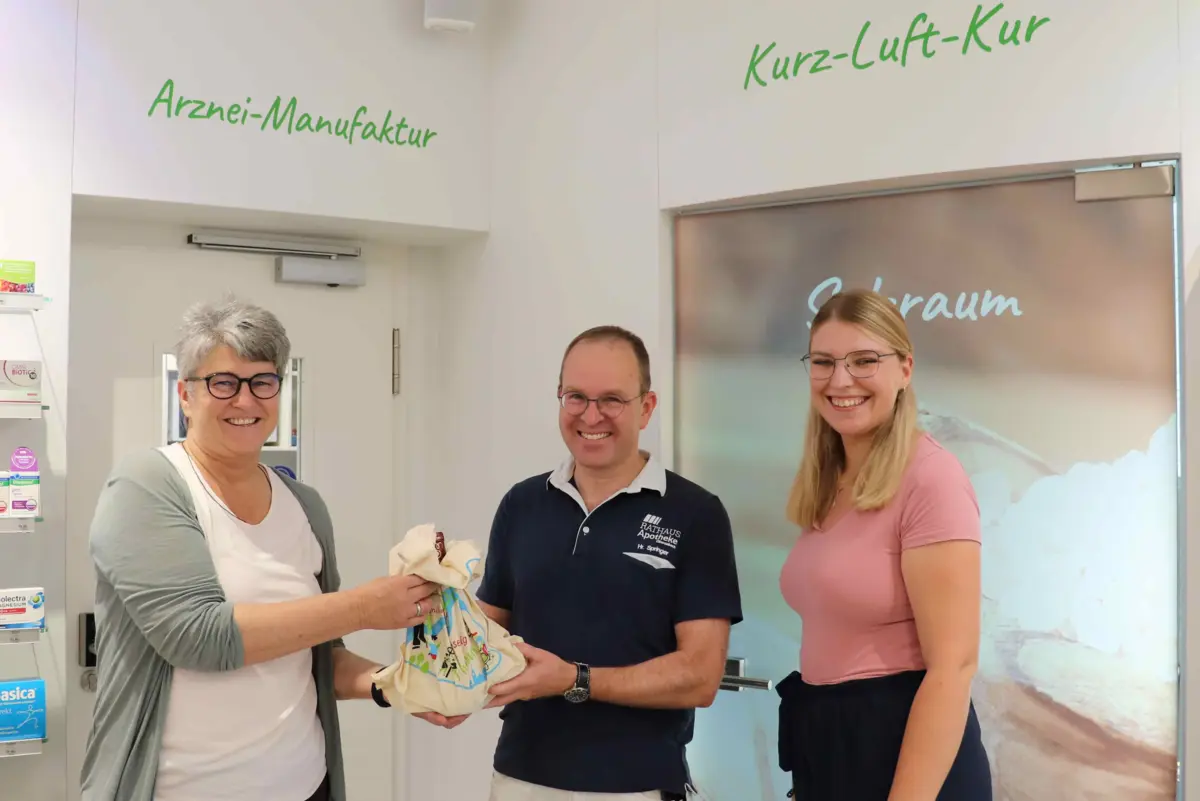 Bürgermeisterin und Mitarbeiterin überreichen Geschenk an Apotheker 