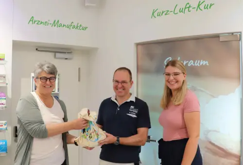 Bürgermeisterin und Mitarbeiterin überreichen Geschenk an Apotheker 