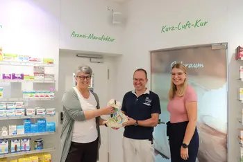 Bürgermeisterin und Mitarbeiterin überreichen Geschenk an Apotheker 