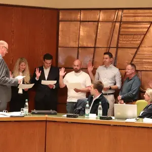 Sechs Männer und eine Frau vor der mit Kupfer beschlagenen Wand des Sitzungssaals
