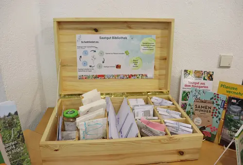 Eine geöffnete Holzkiste mit Sämereien, in deren Deckel eine Beschreibung des Tauschkonzepts angebracht ist