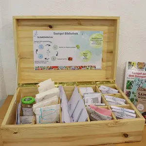 Eine geöffnete Holzkiste mit Sämereien, in deren Deckel eine Beschreibung des Tauschkonzepts angebracht ist