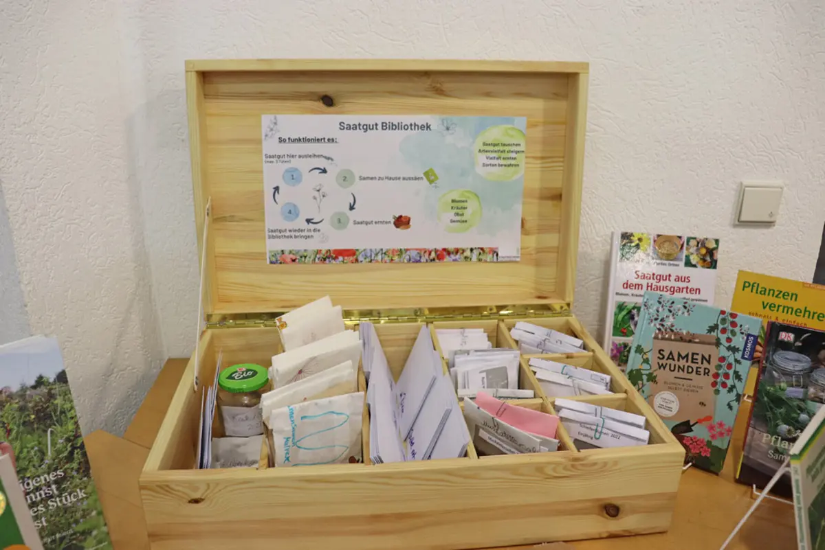 Eine geöffnete Holzkiste mit Sämereien, in deren Deckel eine Beschreibung des Tauschkonzepts angebracht ist