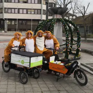 Vier Personen in Plüschhasenkostümen mit zwei Lastenrädern der Stadt Oberasbach vor dem geschmückten Osterbrunnen auf der Südseite des Rathauses. 