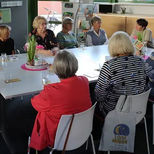 Die ehrenamtlichen Frauen sitzen rund um einen Besprechungstisch und hören der Dozentin gespannt zu.