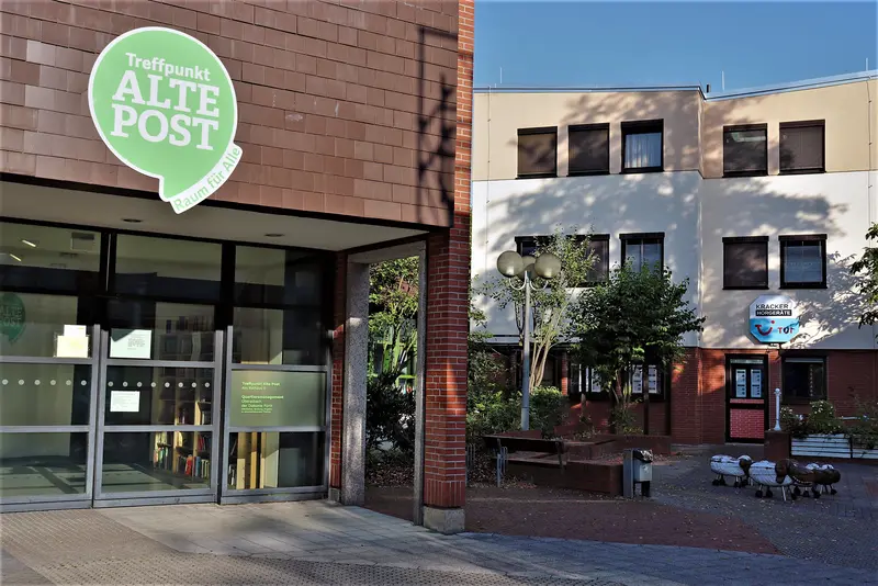 Eingang des Treffpunkts Alte Post: Backsteinbau mit Glastür; über der Tür eine grüne Sprechblase mit weißer Schrift "Treffpunkt Alte Post" 