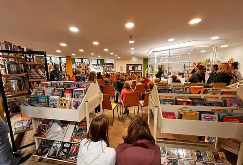 Blick vom Kinder- und Jugendbuchbereich der Stadtbücherei Oberasbach mit zahlreichen von hinten zu sehenden Kindern und rechts einigen Eltern, die Büchereileiterin Edith Backer zuhören 