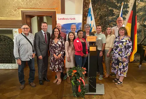 Zahlreiche Männer und Frauen bei der Einbürgerungsfeier mit den Flaggen Deutschlands und Bayerns im Hintergrund 