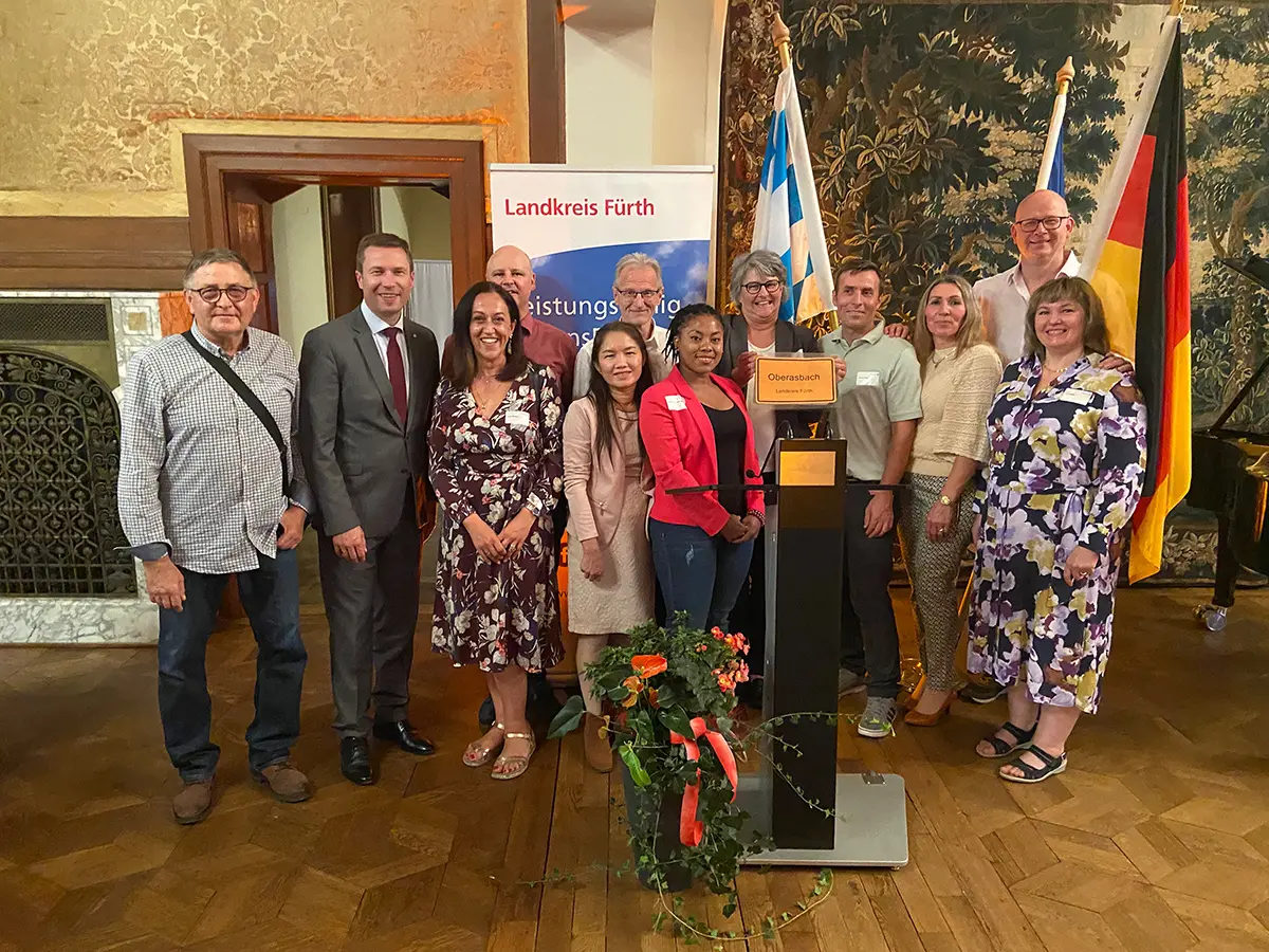 Zahlreiche Männer und Frauen bei der Einbürgerungsfeier mit den Flaggen Deutschlands und Bayerns im Hintergrund 