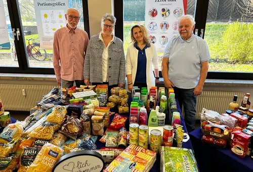 Vier Personen stehen hinter einer reich mit Lebensmitteln gefüllten Tafel