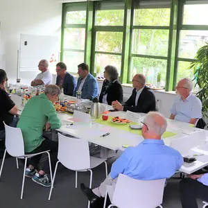 Arbeitstreffen. Die Teilnehmenden schauen auf den Großbildschirm der Videokonferenz.