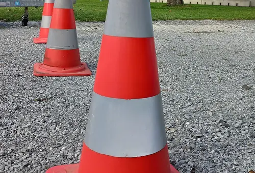 Drei rot-weiße Pylone in Nahaufnahme hintereinander auf einer Straße 