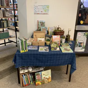 Tisch mit Holzbox für Saatgut, einem Plakat zur Saatgutbörse und vielen Gartenbüchern