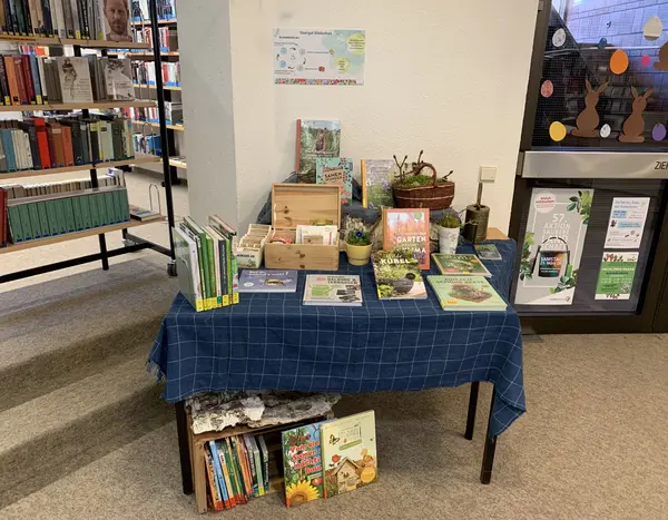 Tisch mit Holzbox für Saatgut, einem Plakat zur Saatgutbörse und vielen Gartenbüchern