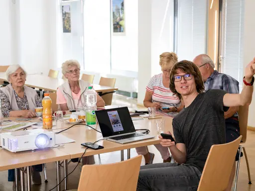 Ein Seminarraum. Vorne erklärt ein Junger Mann mit Laptop etwas. Im Hintegrund sieht man Senioren.