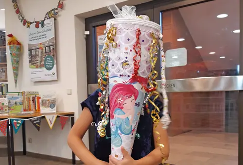 Nahaufnahme eines Mädchens, das sich eine Schultüte mit einer Meerjungfrau vors Gesicht hält