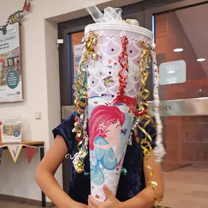 Nahaufnahme eines Mädchens, das sich eine Schultüte mit einer Meerjungfrau vors Gesicht hält