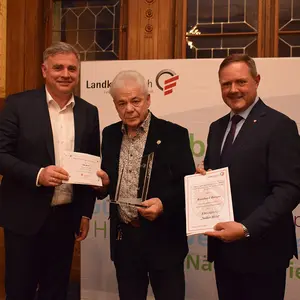 Drei Männer mit Urkunden und Scheck.