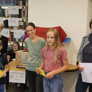 Zwei Kinder bei der Preisübergabe. Im Hintergrund drei Frauen vom Büchereiteam.