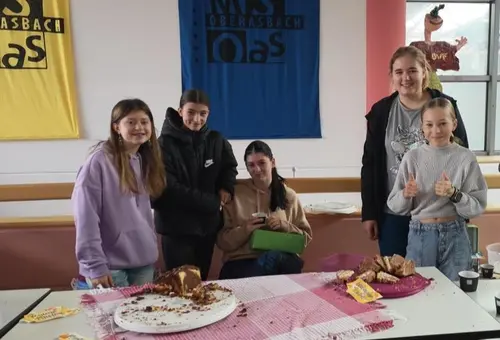 Fünf Mädchen stehen hinter ihrem Verkaufstisch, der mit Kuchen gefüllt ist.