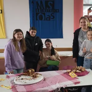 Fünf Mädchen stehen hinter ihrem Verkaufstisch, der mit Kuchen gefüllt ist.