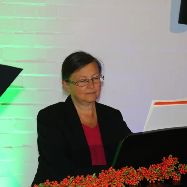 Frau am Klavier. Die Wand im Hintergrund ist grün beleuchtet. 