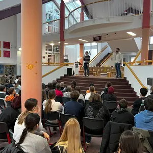 Blick von hinten über die versammelten Kinder zur Empore, auf der zwei Lehrer stehen.
