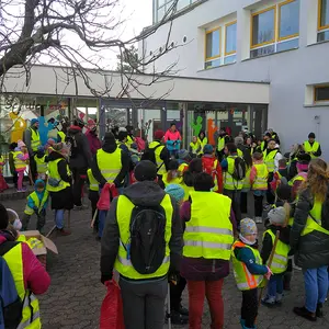 Zahlreiche Erwachsene und KInder mit gelben Warnwesten vor der Schule.