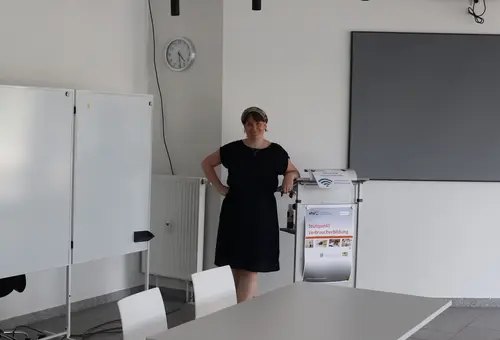 Juliane Braun lehnt am Redernerpult im Schulungsraum. Links ein Whiteboard, rechts hinter ihr eine Projektionsfläche. 
