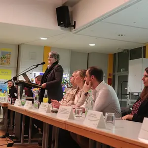 Eine Frau stehend am Podium, daneben rechts und links weitere Personen sitzende von der Verwaltung.