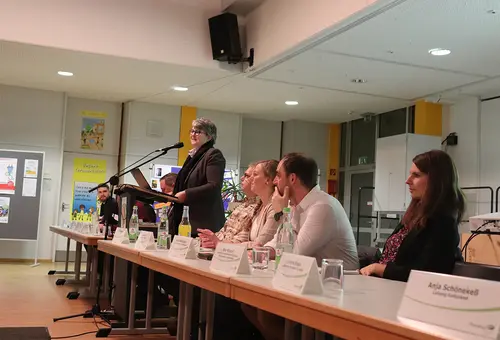 Eine Frau stehend am Podium, daneben rechts und links weitere Personen sitzende von der Verwaltung.