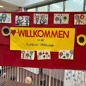 Ein großes Schild in der Aula "Herzlich willkommen" mit Blumen verziert.